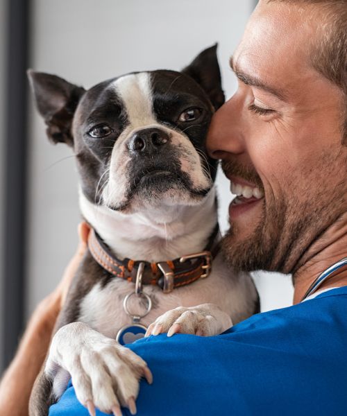 A man smiles while holding a dog in his arms